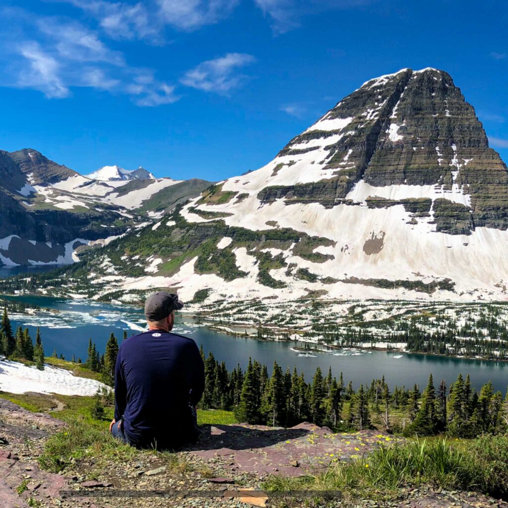 a man sitting on a hill overlooking a lake and mountains