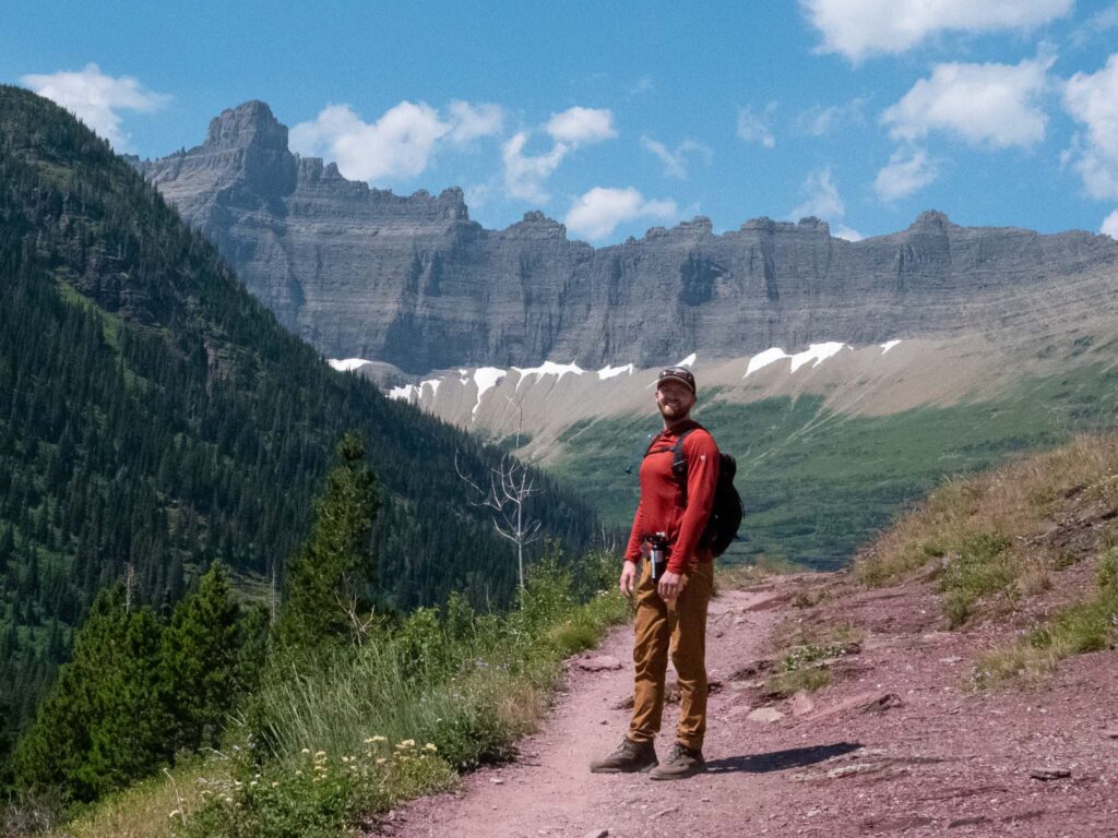 a man standing on a trail with mountains in the background