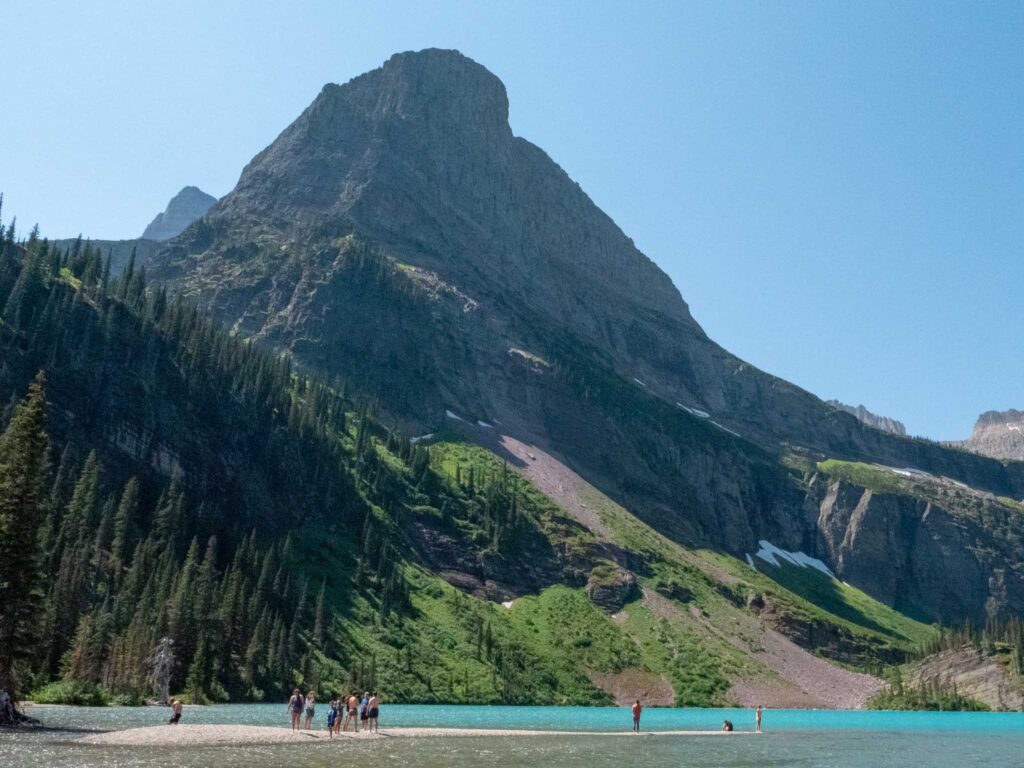 a group of people standing on a beach near a mountain