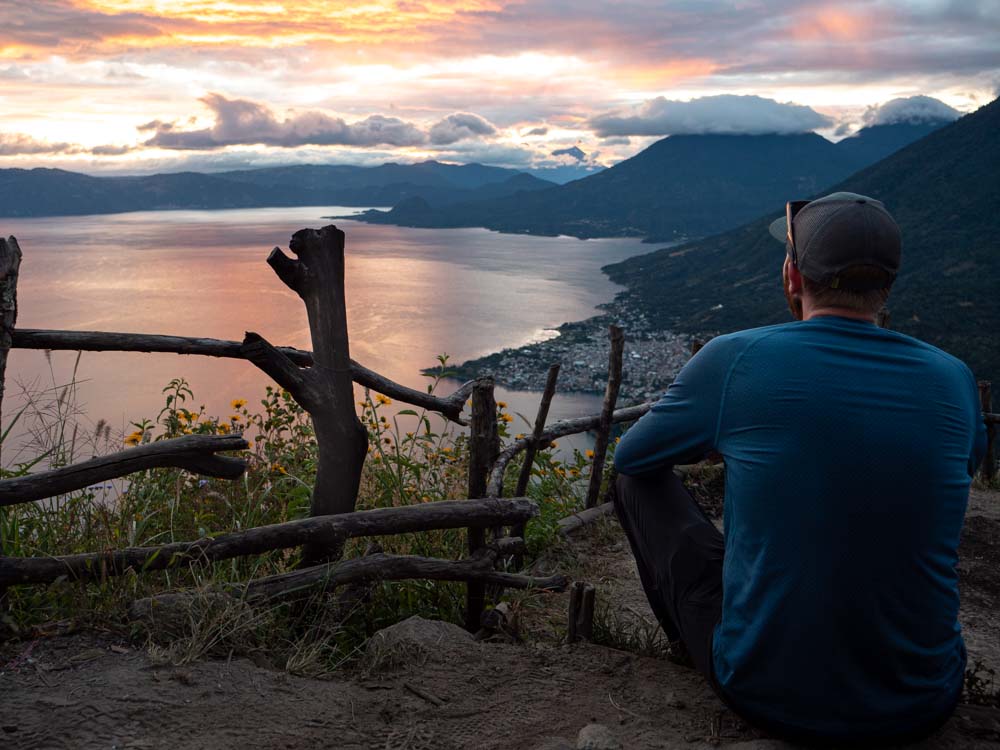 a man sitting on a hill looking at a body of water