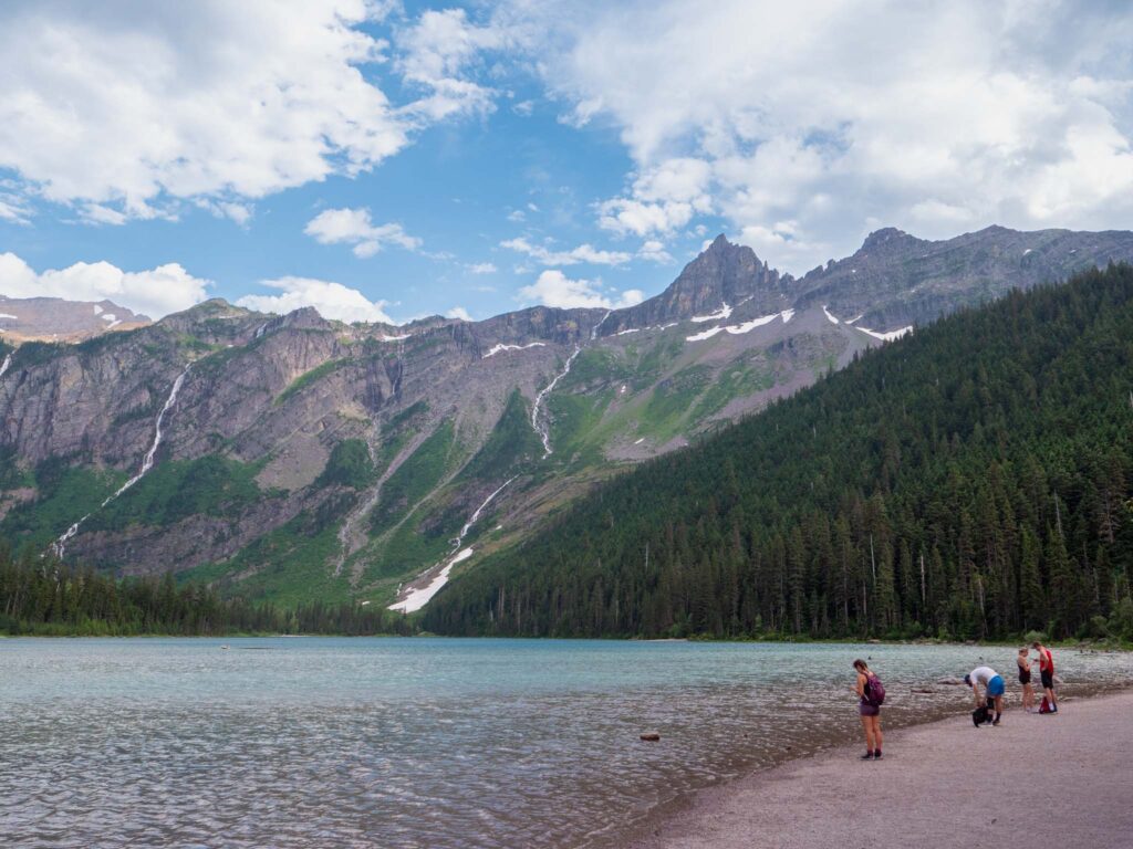 people standing on a beach next to a body of water with mountains in the background