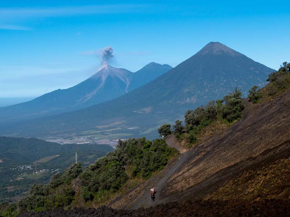 a person on a dirt road with a volcano in the background