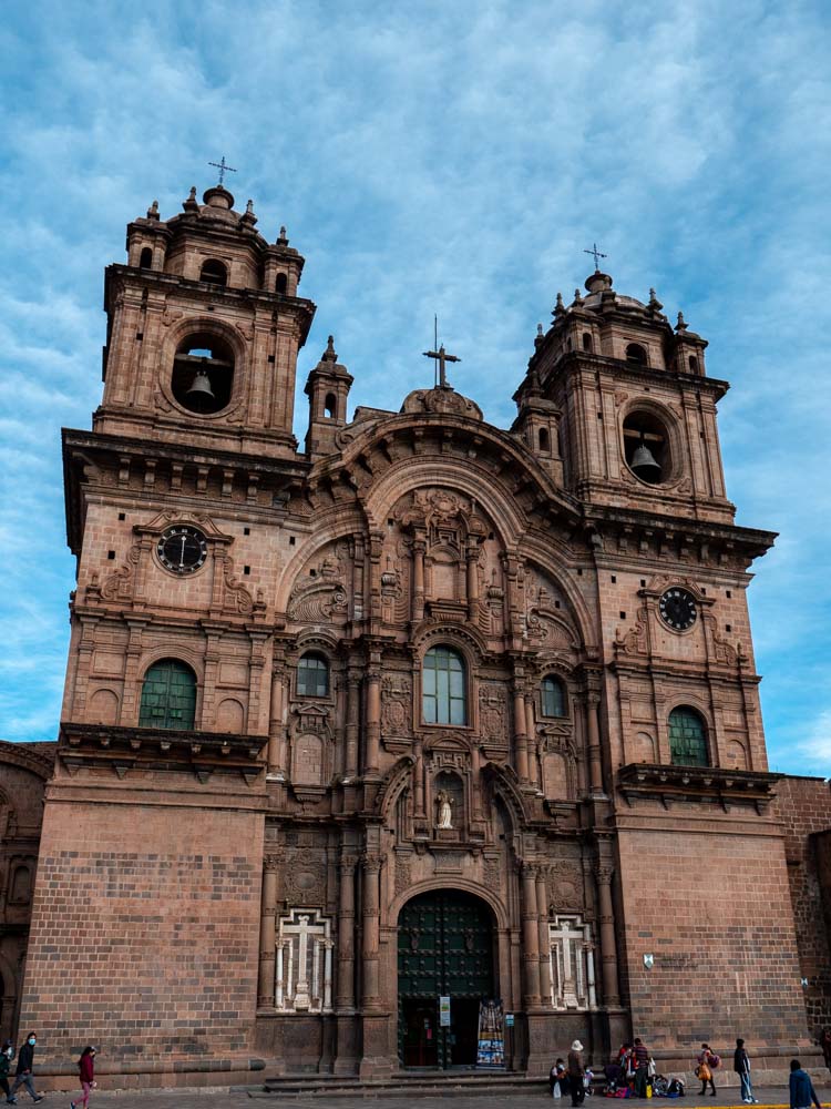 a large building with a large door and a large stone building with Cusco Cathedral in the background