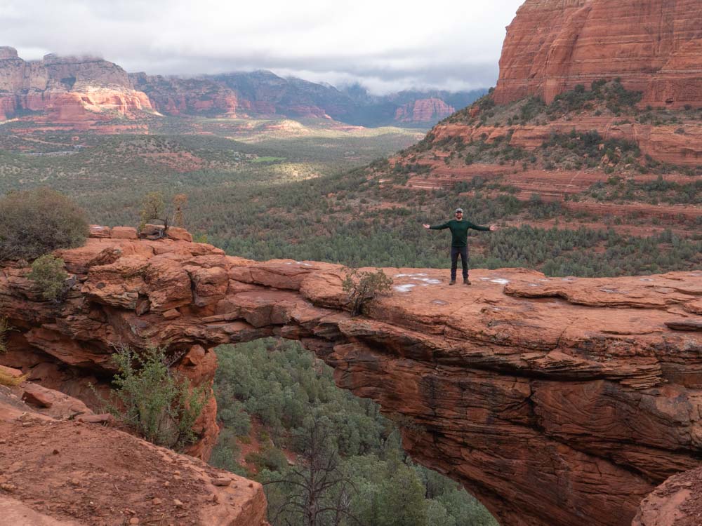 a man standing on a rock bridge with a view of a valley and mountains