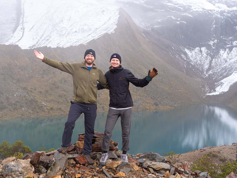 two men standing on rocks with arms outstretched in front of a lake