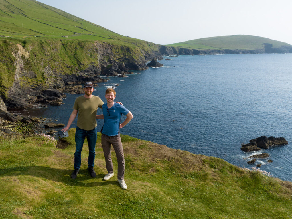 Two men posing near green sea cliffs