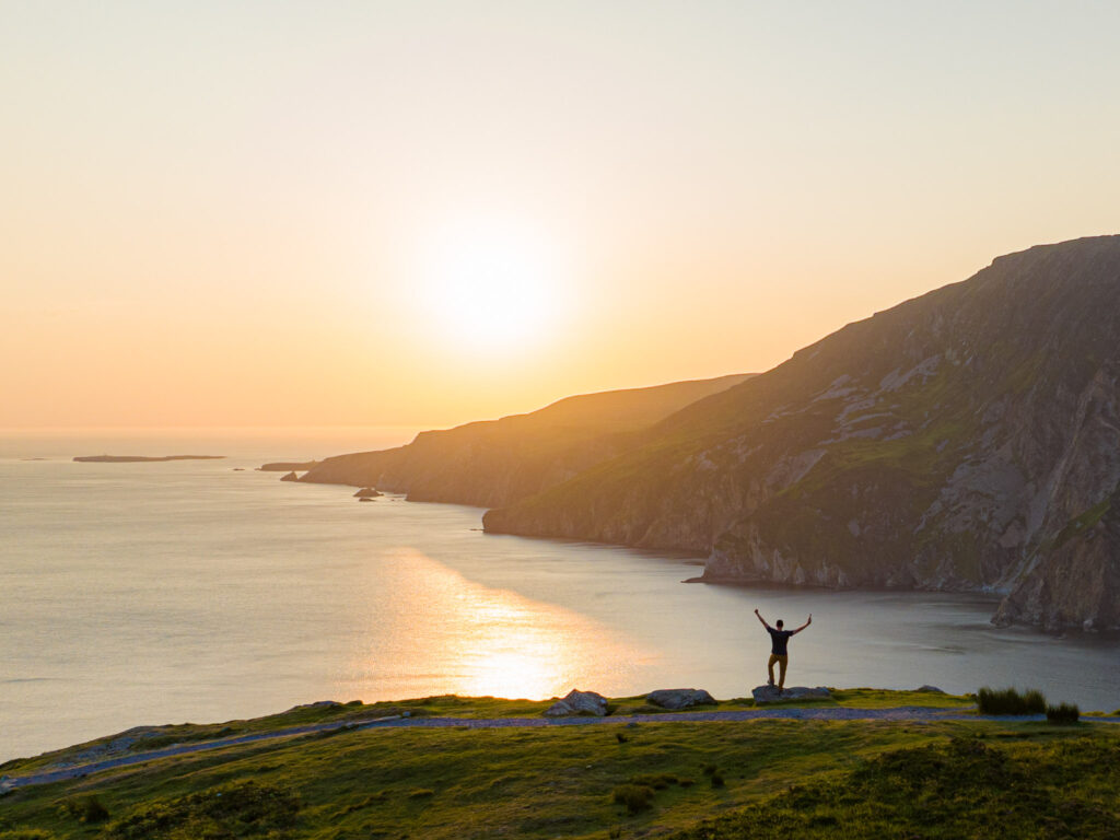 Man standing above ocean cliffs during sunset