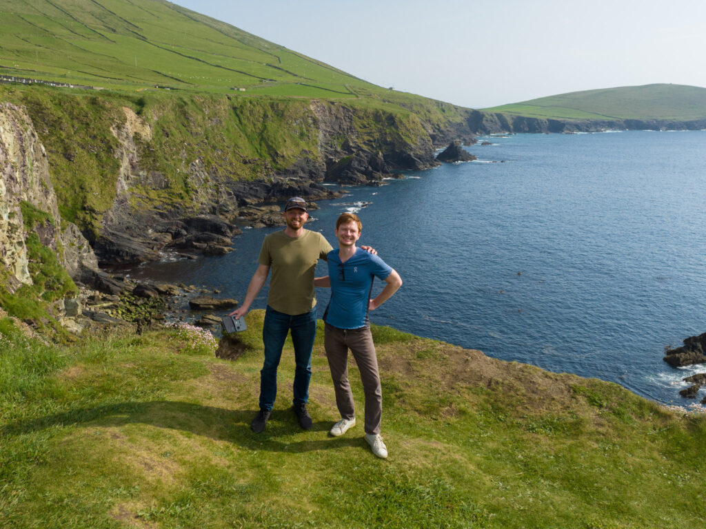 Two men posing for a photo along vibrant green coastal cliffs