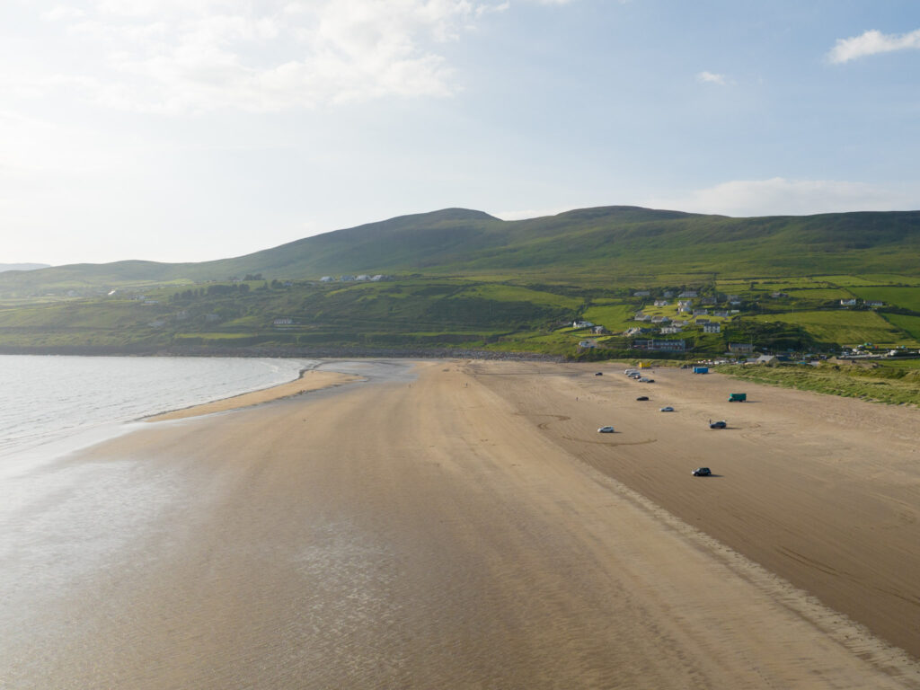 Massive beach with cars parked in the sand and mountain background