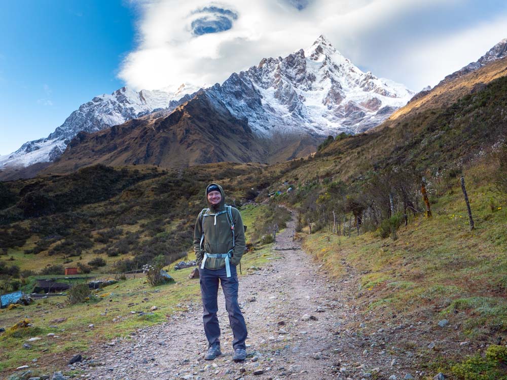 a man standing on a dirt path with a snowy mountain in the background