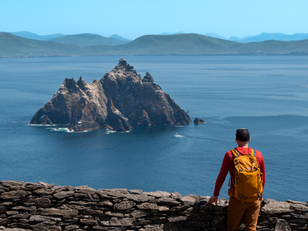 a man standing on a stone wall overlooking a large rock island