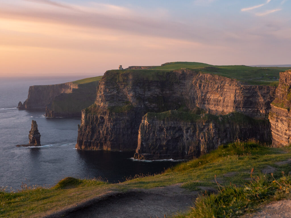 a large cliff with grass and water in the background with Cliffs of Moher in the background