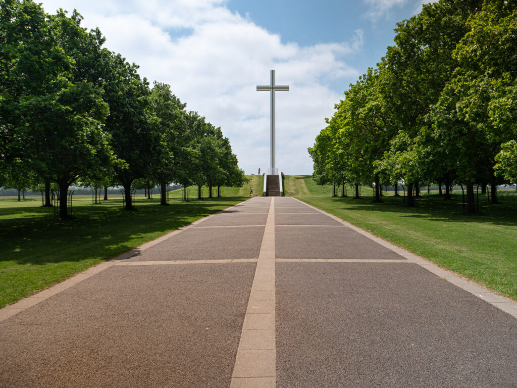 A sidewalk leading up to a large cross lined with trees