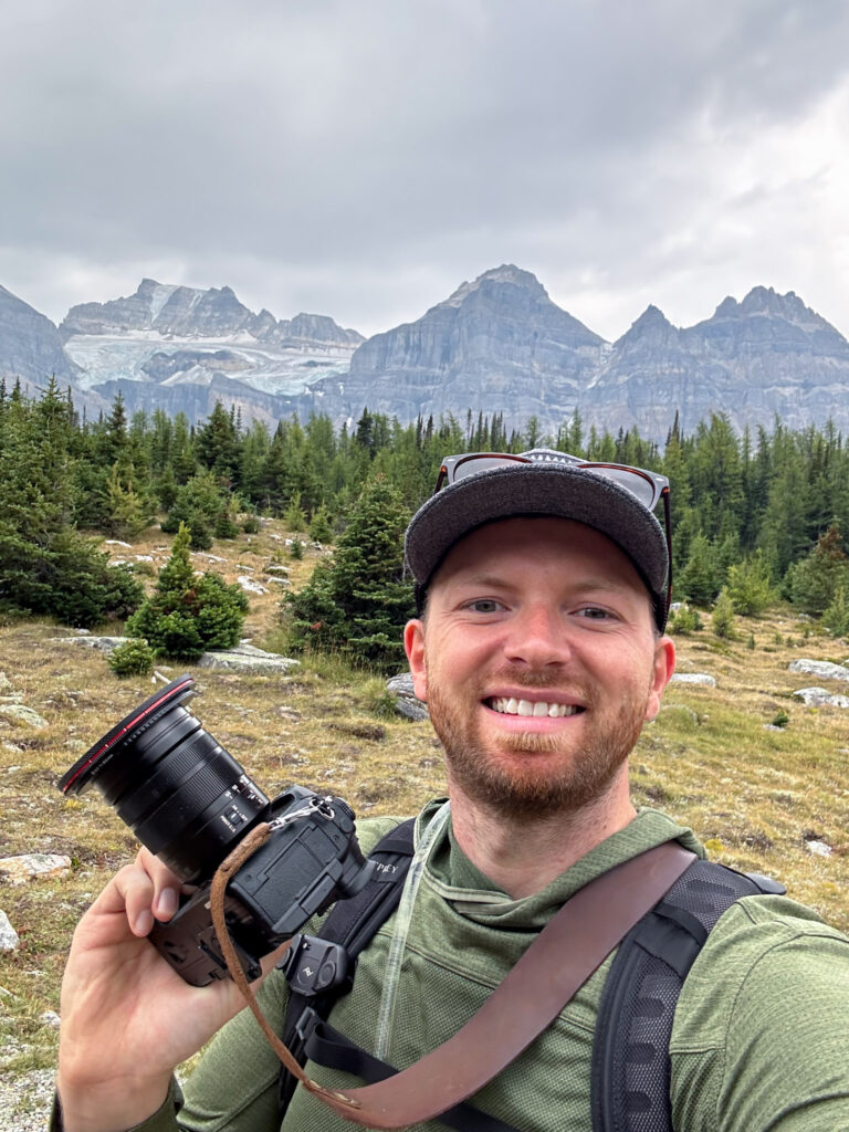 a man taking a selfie with a camera in front of mountains