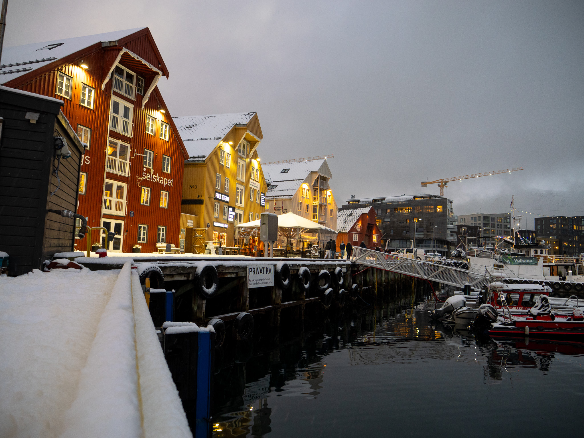 a snow covered dock with buildings and boats in the water