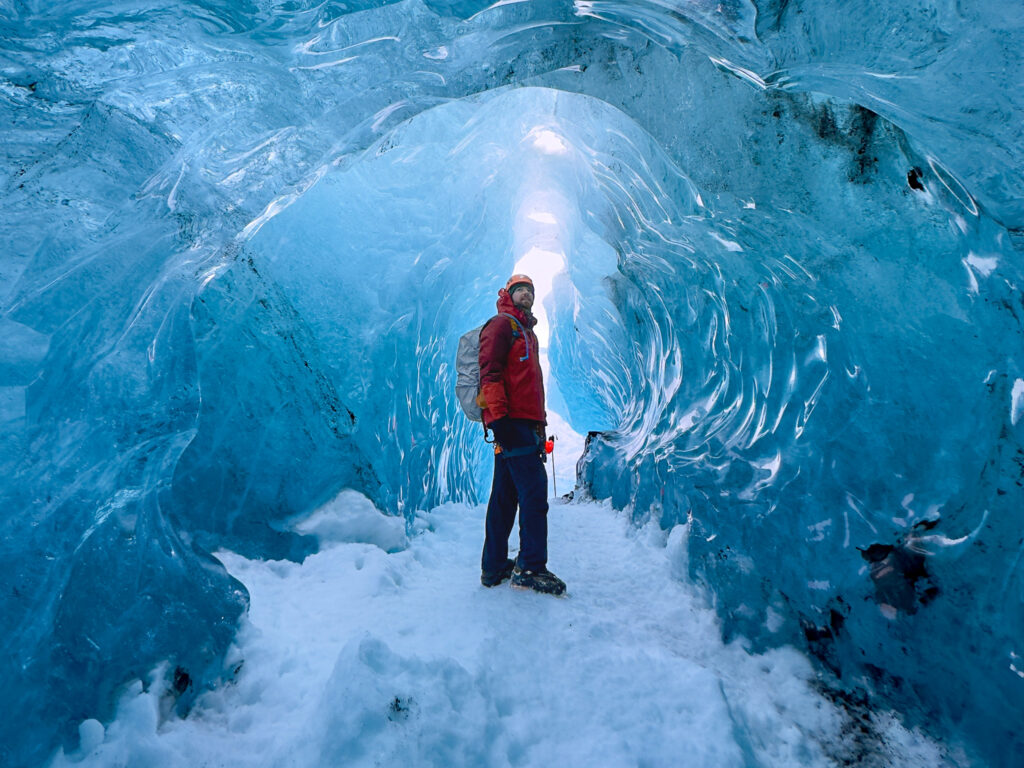 Hiker standing in a blue glacial ice cave