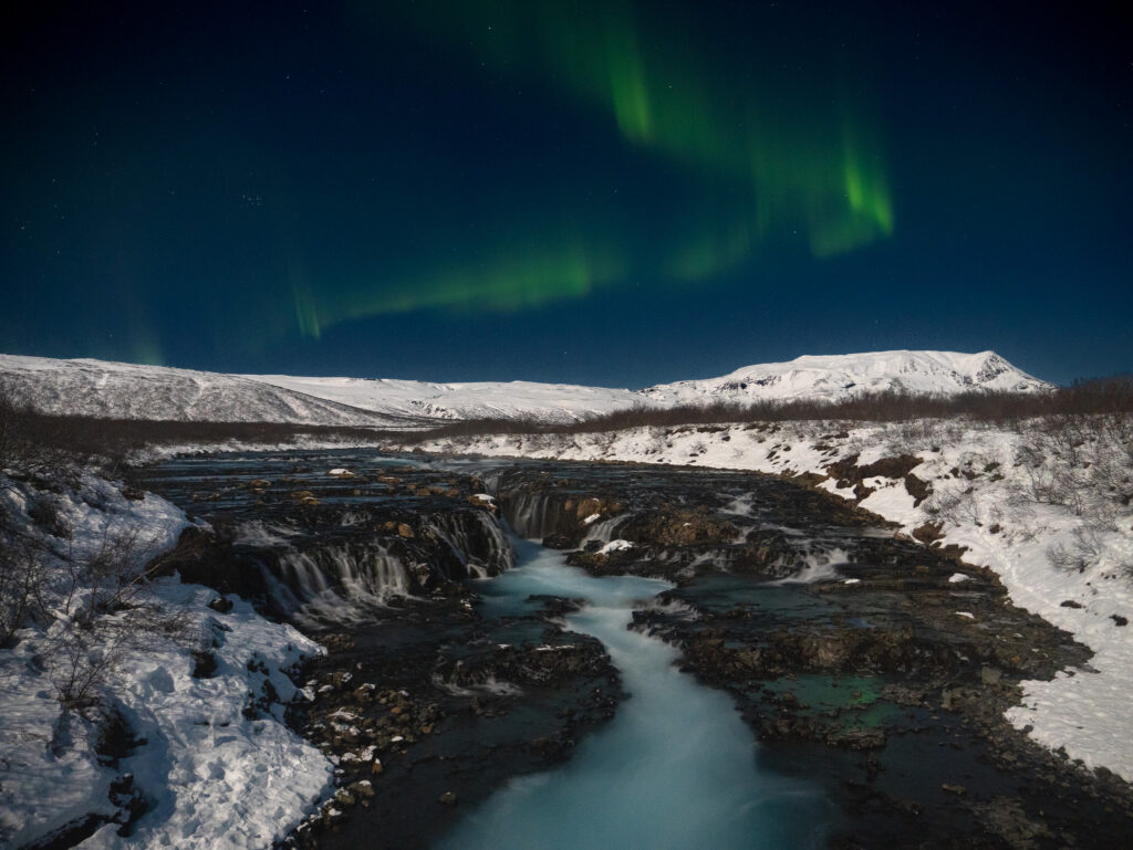 Northern Lights display above the Bruarfoss waterfall at night in Iceland