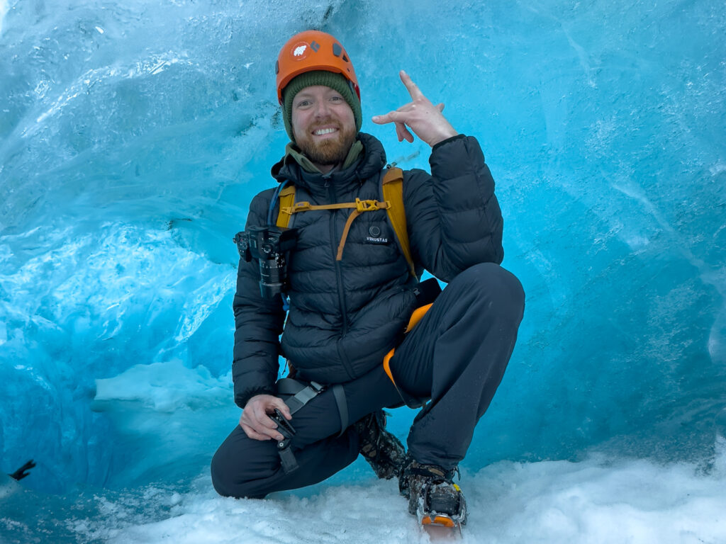 Hiker in black coat posing in a blue ice cave