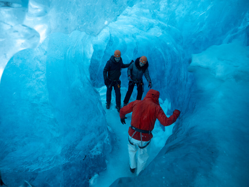 Glacier guide helping two hikers inside a blue ice cave