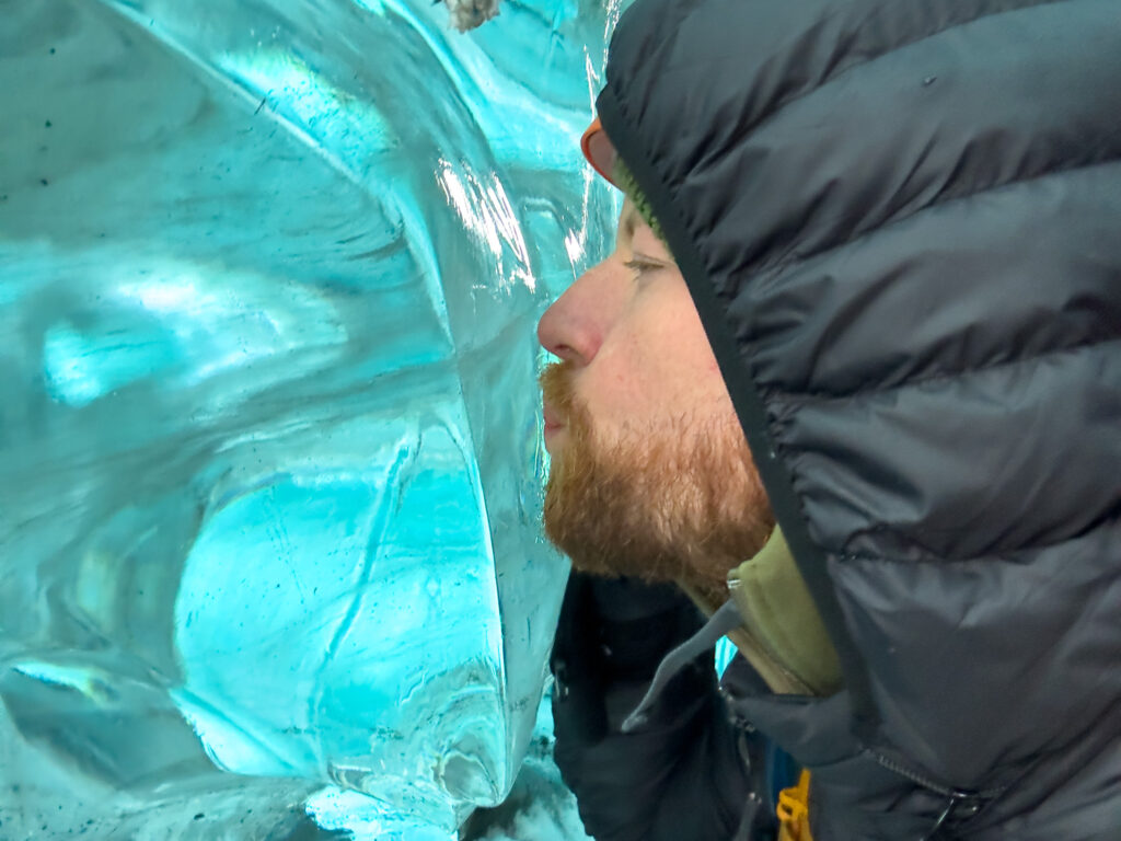 Man kissing the blue wall of a glacial ice cave