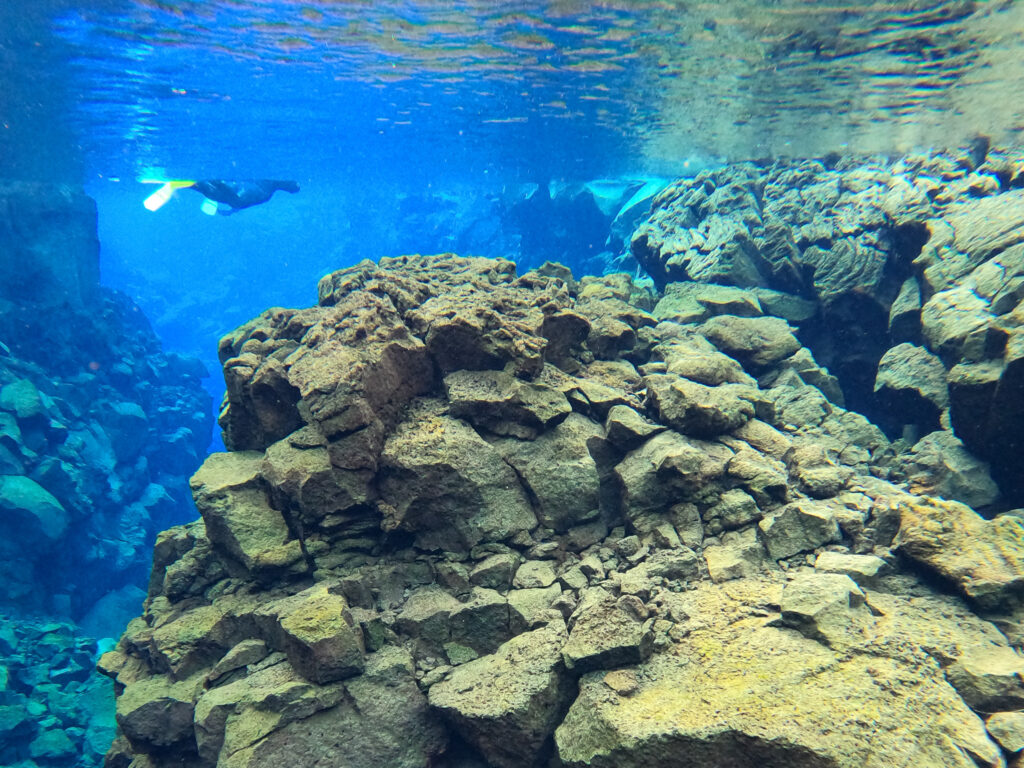 Large rock formations near a snorkeler in the Silfra Fissure