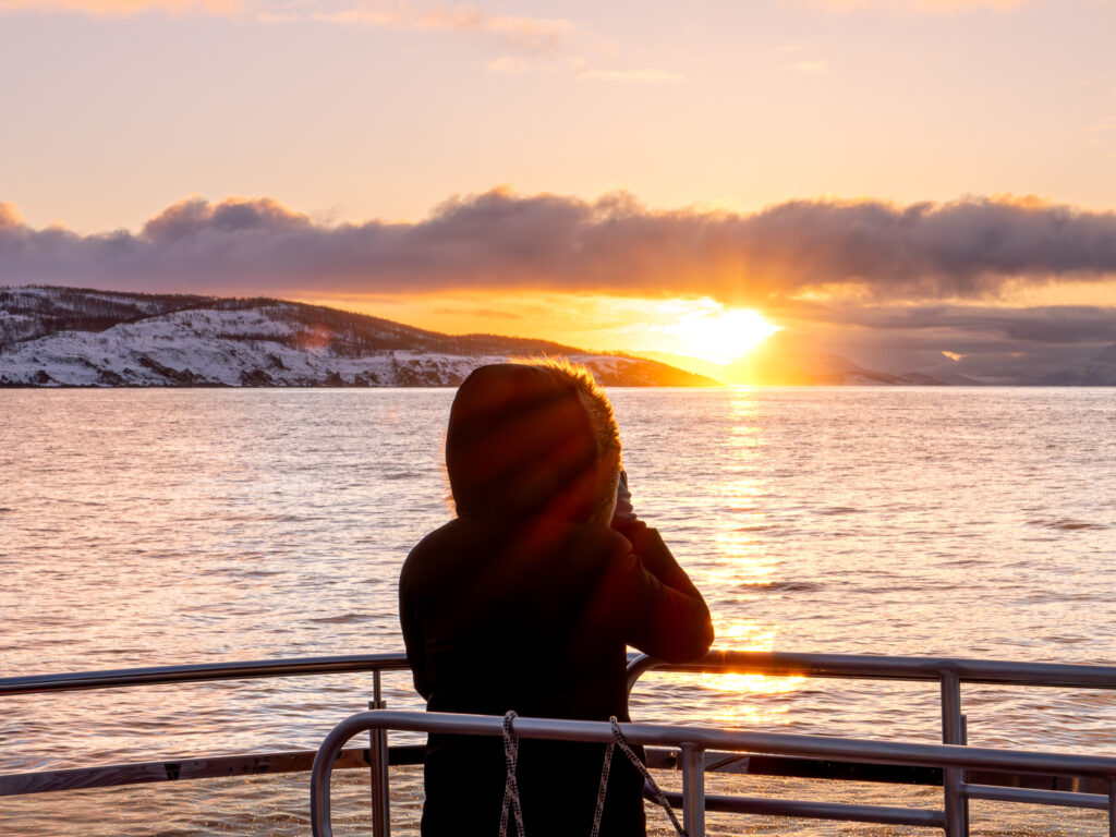 a person standing on a boat looking at the sunset