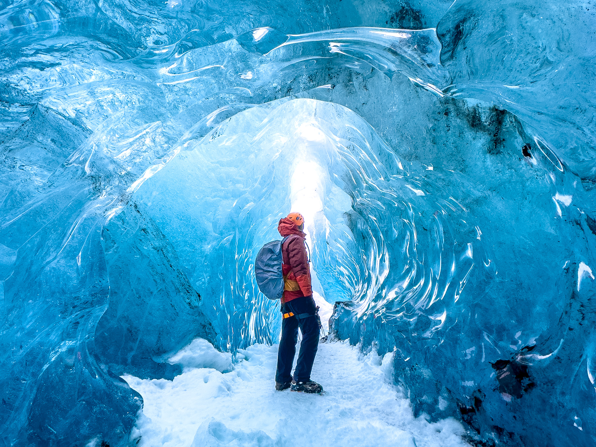 Man looking into the bright light standing in a blue glacier ice cave