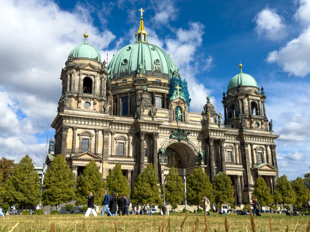 a large building with green domes and people walking in front with Berlin Cathedral in the background